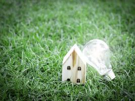 casa in legno e lampadina su erba verde, risparmio energetico, utilizzo di energia verde rinnovabile per salvare il mondo, amare e proteggere il nostro pianeta, concetto rispettoso dell'ambiente foto