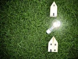 casa in legno e lampadina su erba verde, risparmio energetico, utilizzo di energia verde rinnovabile per salvare il mondo, amare e proteggere il nostro pianeta, concetto rispettoso dell'ambiente foto