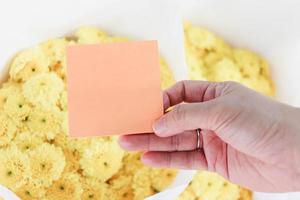 carta per appunti vuota in mano su bellissimi crisantemi gialli bouquet di fiori sfondo, copia-spazio su carta per mettere il tuo messaggio. foto