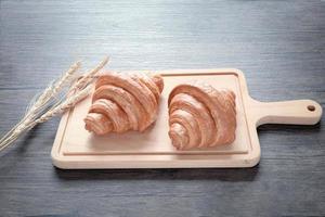 due deliziosi croissant appena sfornati con spighette sul tagliere di legno, cibo sul tavolo della colazione foto