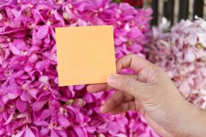 carta per appunti vuota in mano su un bellissimo sfondo rosa viola bouquet di fiori di orchidea, copia-spazio su carta per mettere il tuo messaggio. foto