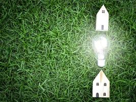 casa in legno e lampadina su erba verde, risparmio energetico, utilizzo di energia verde rinnovabile per salvare il mondo, amare e proteggere il nostro pianeta, concetto rispettoso dell'ambiente foto