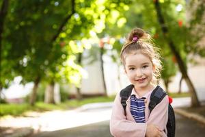 una bambina di aspetto caucasico in uniforme scolastica con uno zaino guarda nell'inquadratura. concetto di ritorno a scuola. la prima classe, sviluppando attività per bambini in età prescolare. spazio per il testo foto