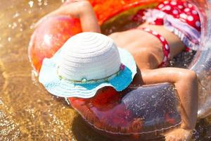 ragazza con un cappello che nuota nel fiume con un cerchio gonfiabile trasparente a forma di cuore con piume arancioni all'interno.il mare con un fondo sabbioso. vacanze al mare, nuoto, abbronzatura, creme solari. foto