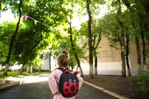 una bambina di razza caucasica in uniforme scolastica con uno zaino guarda la strada nel cortile della scuola. concetto di ritorno a scuola. scuola elementare, sviluppando attività per bambini in età prescolare. spazio per il testo foto