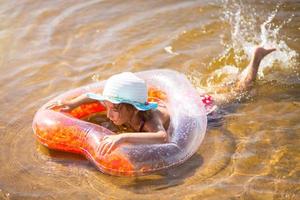 ragazza con un cappello che nuota nel fiume con un cerchio gonfiabile trasparente a forma di cuore con piume arancioni all'interno.il mare con un fondo sabbioso. vacanze al mare, nuoto, abbronzatura, creme solari. foto