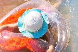 ragazza con un cappello che nuota nel fiume con un cerchio gonfiabile trasparente a forma di cuore con piume arancioni all'interno.il mare con un fondo sabbioso. vacanze al mare, nuoto, abbronzatura, creme solari. foto