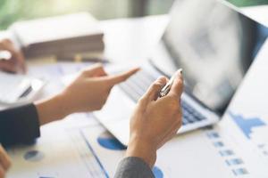 primo piano delle mani di due uomini e donne che indossano abiti casual che lavorano con i grafici su un tavolo bianco e prendono appunti. inquadratura ravvicinata in tempo reale bloccata foto