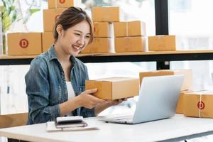 piccola impresa imprenditrice di giovani donne asiatiche che lavorano con il computer portatile per lo shopping online a casa, allegra e felice con la scatola per l'imballaggio a casa, avviare un'attività in proprio per l'attività online foto