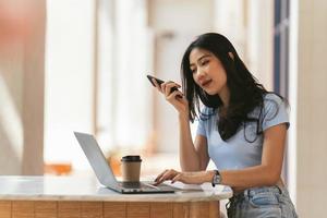 la donna asiatica in abiti casual è felice e allegra mentre comunica con il suo smartphone e lavora in una caffetteria. foto