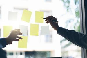 uomini d'affari che si incontrano in ufficio e usano post-it per condividere un'idea. concetto di brainstorming. nota adesiva sulla parete di vetro. foto