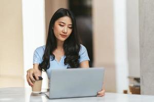 ritratto di giovane donna asiatica che lavora al computer portatile e relazione finanziaria alla caffetteria. foto