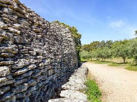 stretto sentiero tra un muro e alberi in una giornata di sole foto