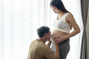 giovane donna incinta con il marito che abbraccia e aspetta un bambino a casa foto