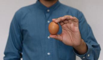 mano maschio che tiene uovo di gallina marrone di pasqua isolato su sfondo grigio foto