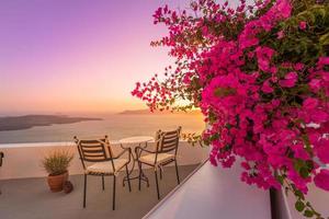 bella vista della caldera e godersi uno scenario romantico tramonto sul mar egeo, santorini. vacanza di viaggio di coppia, destinazione per la luna di miele. romanticismo con fiori, due sedie tavolo e vista mare. vacanza di lusso foto