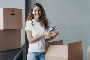 felice donna europea che disimballa scatole e toglie libri e appunti. giovane studente nella stanza del campus. foto