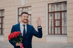 bel giovane vestito con un mazzo di rose che saluta il suo socio in affari con un mazzo di rose rosse foto