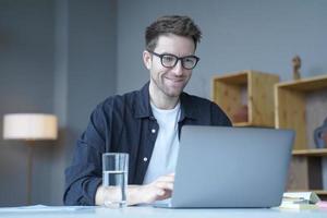 giovane uomo d'affari sorridente consulente finanziario europeo che lavora in remoto online dall'ufficio di casa foto
