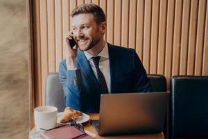 sorridente uomo d'affari con la barba lunga in abito formale che parla al cellulare nella caffetteria foto