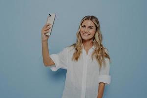giovane donna sorridente allegra con lunghi capelli biondi ondulati che fa foto sullo smartphone