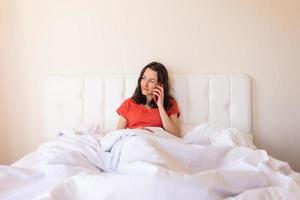 una donna si siede su un letto e chiama al telefono foto