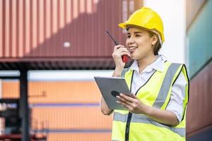 giovane ingegnere o manager asiatico in possesso di un tablet e uso della comunicazione radio per controllare il carico del container nei concetti di trasporto industriale e logistica foto