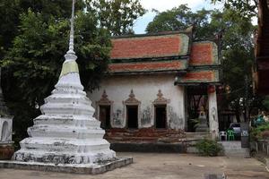 stupa bianco accanto all'antica chiesa nativa nel tempio buddista e circondato da alberi, la base della chiesa è rotta e si aprono alcuni mattoni rossi, bangkok, thailandia. foto