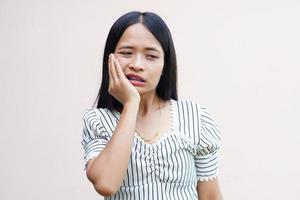 donna asiatica con mal di denti si preme la mano sul viso foto