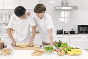giovane coppia asiatica maschio lgbt felice di trascorrere del tempo insieme durante la cottura dell'insalata di pane in cucina bianca con la faccia sorridente. messa a fuoco selettiva. foto