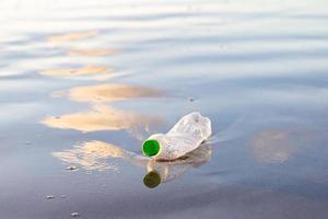 ridurre l'uso di bottiglie di plastica, riciclando la bottiglia di plastica vuota usata. una bottiglia di plastica scartata viene lavata su una spiaggia sabbiosa. ecologia, protezione della terra, conservazione della natura, inquinamento del mare. foto