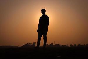 silhouette uomo, in piedi su un campo rurale e guardando dritto. sagoma di un uomo con vista tramonto su un campo. concetto di natura con una vista del tramonto e un ragazzo in piedi silhouette fotografia ravvicinata. foto
