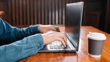 mano dell'uomo che lavora utilizzando il laptop a casa mentre è seduto a una scrivania in legno mano maschile digitando sulla tastiera del notebook foto
