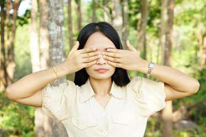 le donne asiatiche si coprono gli occhi con entrambe le mani sullo sfondo della natura foto