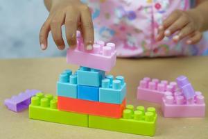 le mani della bambina stanno giocando sul tavolo con uno smontaggio di un blocco giocattolo, girato in studio foto