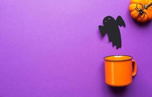 tazza arancione su sfondo viola con terribili decorazioni di Halloween. il concetto della vacanza di halloween. bevanda, divertimento, festa. copia spazio, mock up, in modo piatto foto