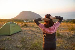 la donna incontra l'alba in montagna, gioisce al sole. vista panoramica sulla montagna e sul mare dall'alto. campeggio, attività all'aperto, escursionismo sportivo in montagna, viaggi in famiglia. ayu-dag, Crimea. foto