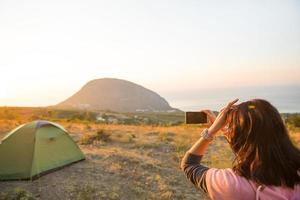 la donna scatta foto dell'alba in montagna sul suo telefono. selfie al sorgere del sole. vista panoramica sul mare e ayu-dag. campeggio, attività all'aperto, escursionismo sportivo in montagna, viaggi in famiglia. Crimea.