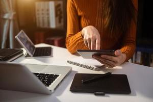 donna che utilizza lo smartphone per pagamenti mobili acquisti online, canale omni, seduto sul tavolo, schermo dell'interfaccia grafica icone virtuali foto