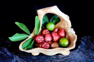 agrumi e guava con foglie in contenitori di legno, fondo nero foto