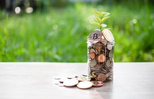 bitcoin e altre monete in una bottiglia di vetro sono posti su un tavolo di legno e il sole del mattino splende. ci sono molte monete nel salvadanaio. valuta digitale dei soldi di concetto. primo piano, sfondo sfocato foto