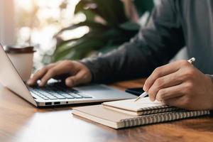 gli uomini d'affari lavorano al computer e scrivono sul blocco note con una penna per calcolare i rendiconti finanziari all'interno dell'azienda. foto