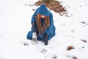 giovane donna in cappotto blu retrò a piedi nel parco nebbioso nei periodi invernali, neve e alberi sullo sfondo, fantasia o concetto di fata foto