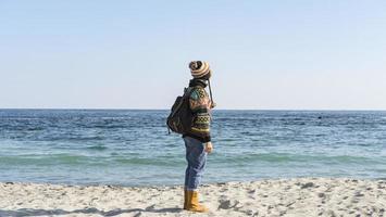 una ragazza con un maglione colorato e un cappello cammina sulla spiaggia soleggiata autunnale foto