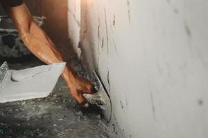 primo piano del lavoratore che intonaca un muro di cemento per la costruzione di una casa foto