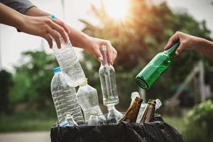 le persone tengono in mano una bottiglia di immondizia in plastica e vetro che mettono nel sacchetto di riciclaggio per la pulizia foto