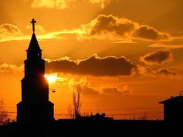 una chiesa in piedi davanti a un sole al tramonto foto