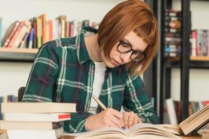 giovane donna rossa con gli occhiali legge il libro in biblioteca foto