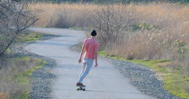 giovane maschio giro su skateboard longboard sulla strada di campagna in una giornata di sole foto