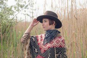 giovane viaggiatrice in poncho e cappello cammina nei campi e nella fattoria foto